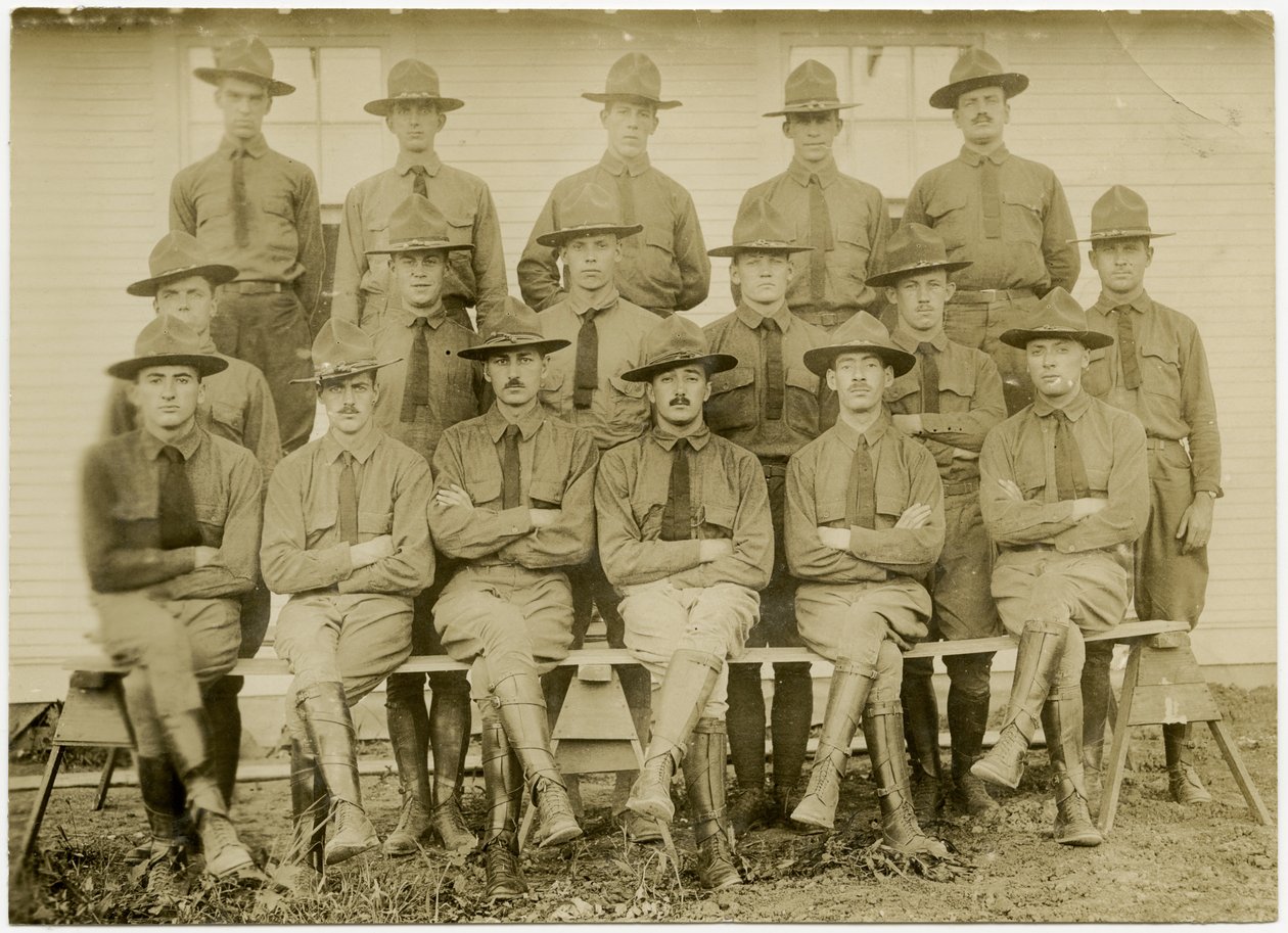 Horizontale, sepiafarbene Fotografie einer Gruppe von siebzehn uniformierten Soldaten, die für ein Gruppenfoto posieren. Die Soldaten sind in drei Reihen aufgeteilt; eine Reihe sitzt vorne, eine Reihe steht in der Mitte und eine Reihe steht auf einer Platt von Carl Michel