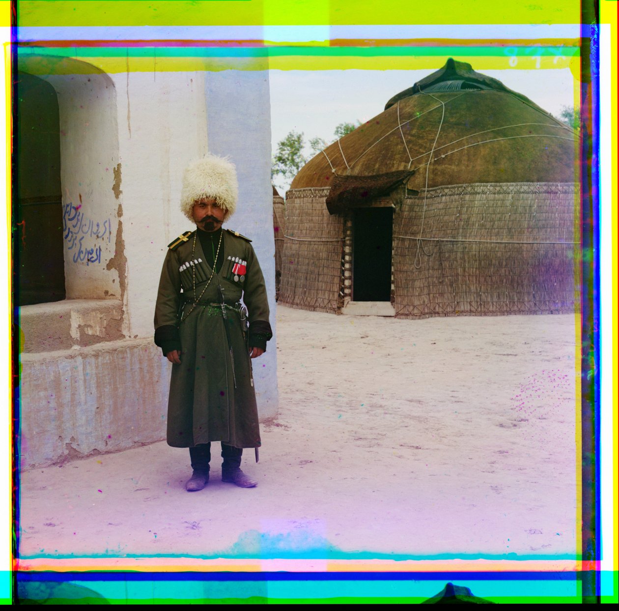 Ein bewaffneter Mann in Uniform steht neben einem Gebäude mit einer Jurte im Hintergrund, Russland, 1915 von Sergey Prokudin Gorsky