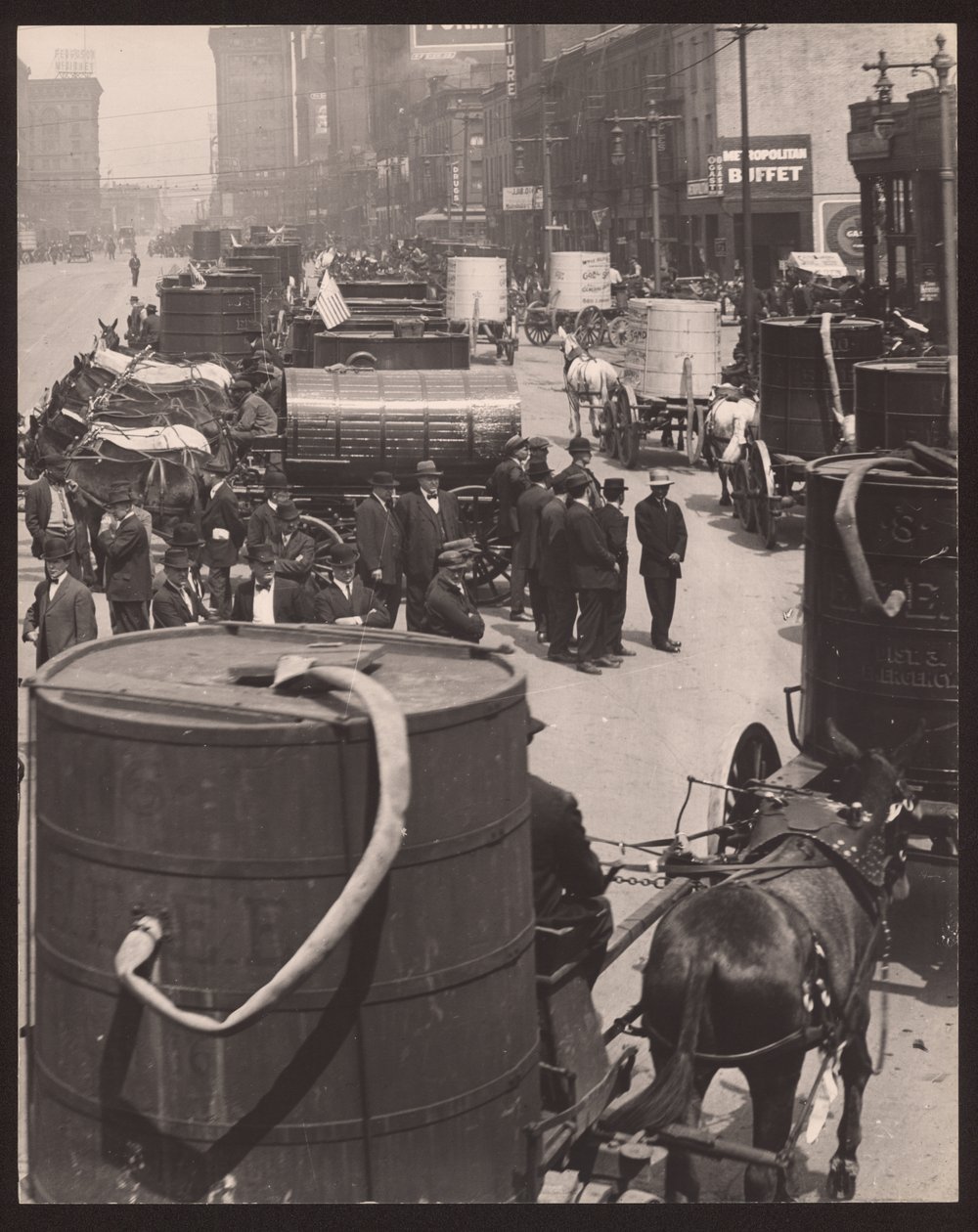 Vertikales, schwarz-weißes Foto einer Reihe von pferdegezogenen Wagen mit Wasserfässern. Eine Gruppe von Männern steht vor der Reihe von William G. Swekosky